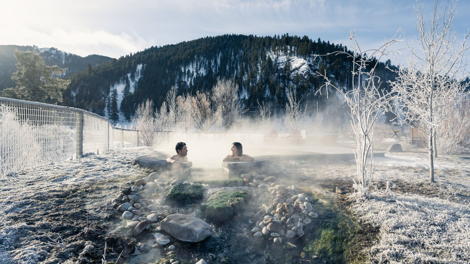 A couple relaxes in Astoria Hot Springs during a gorgeous winter day in Jackson Hole.