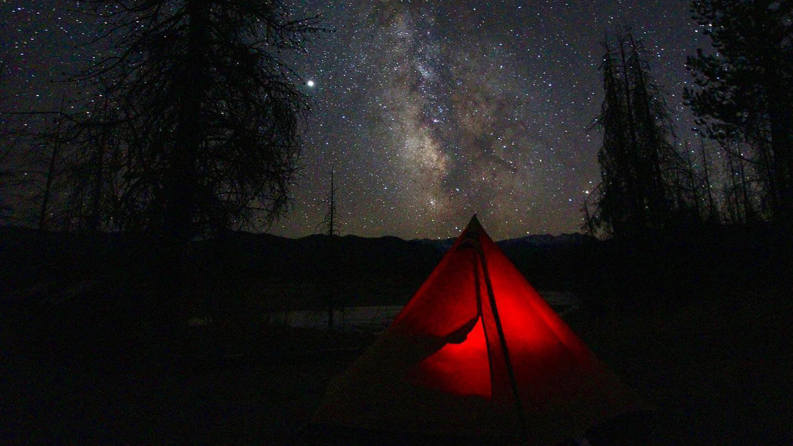 Red tent lit up under a starry night sky.