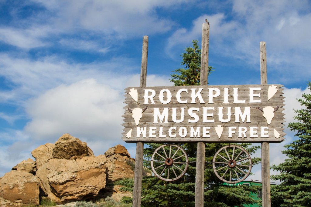A wooden sign that reads, "Rockpile Museum - Welcome - Free" in front of a group of trees and pile of rocks at the Rockpile Museum.