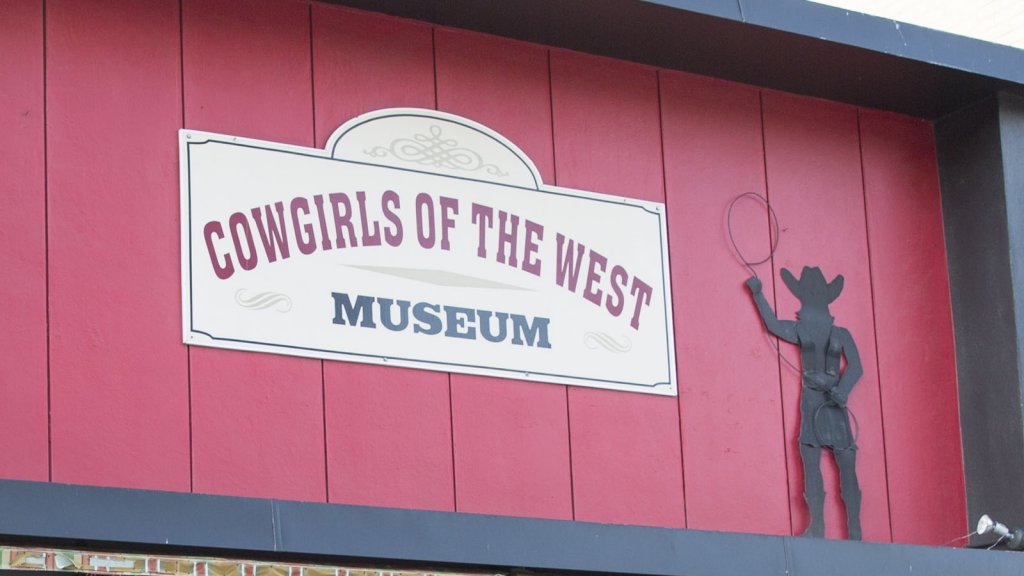 Sign for Cowgirls of the West, a muse-see museum in Wyoming, with a cartoon figure of a cowgirl lassoing.