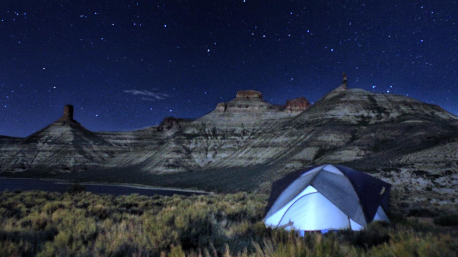 A tent glows from a campsite at the Flaming Gorge Reservoir, where bright stars beam, twinkling above. 