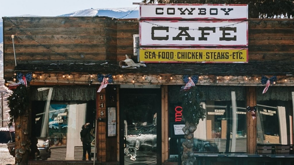 An outside view of the wooden Cowboy Cafe building and a sign that says Cowboy Cafe Sea Food Chicken Steaks Etc.