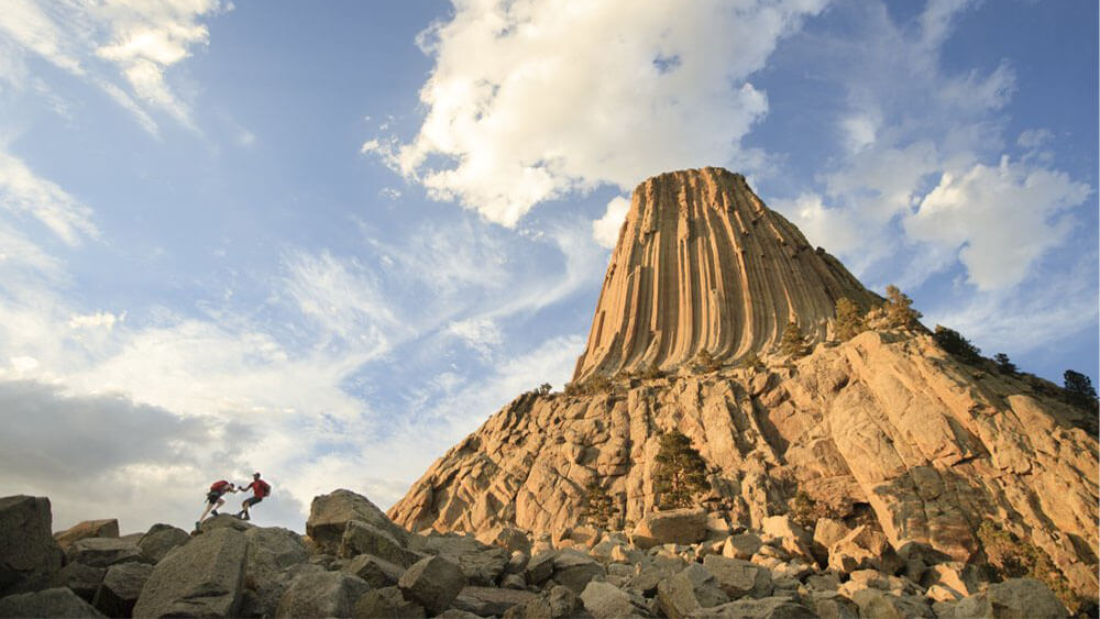 hikers scaling Devils Tower National Monument, a Wyoming getaway spot.