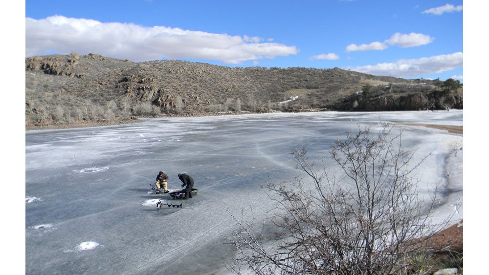 Two fishermen on a frozen lake drilling for an ice fishing hole in Curt Gowdy State Park.