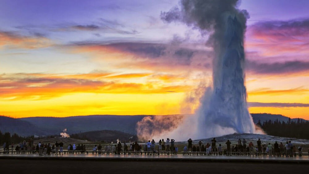 Onlookers viewing Old Faithful geyser at Yellowstone National Park during the summer.