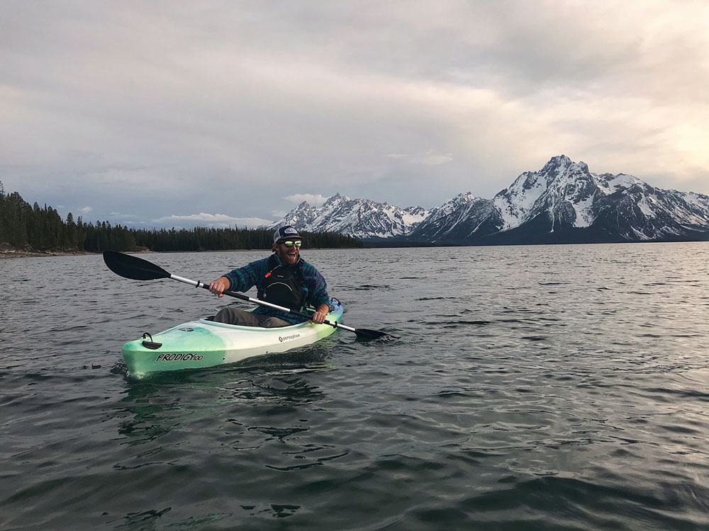Kayaker on a lake, snow covered mountains in the background.