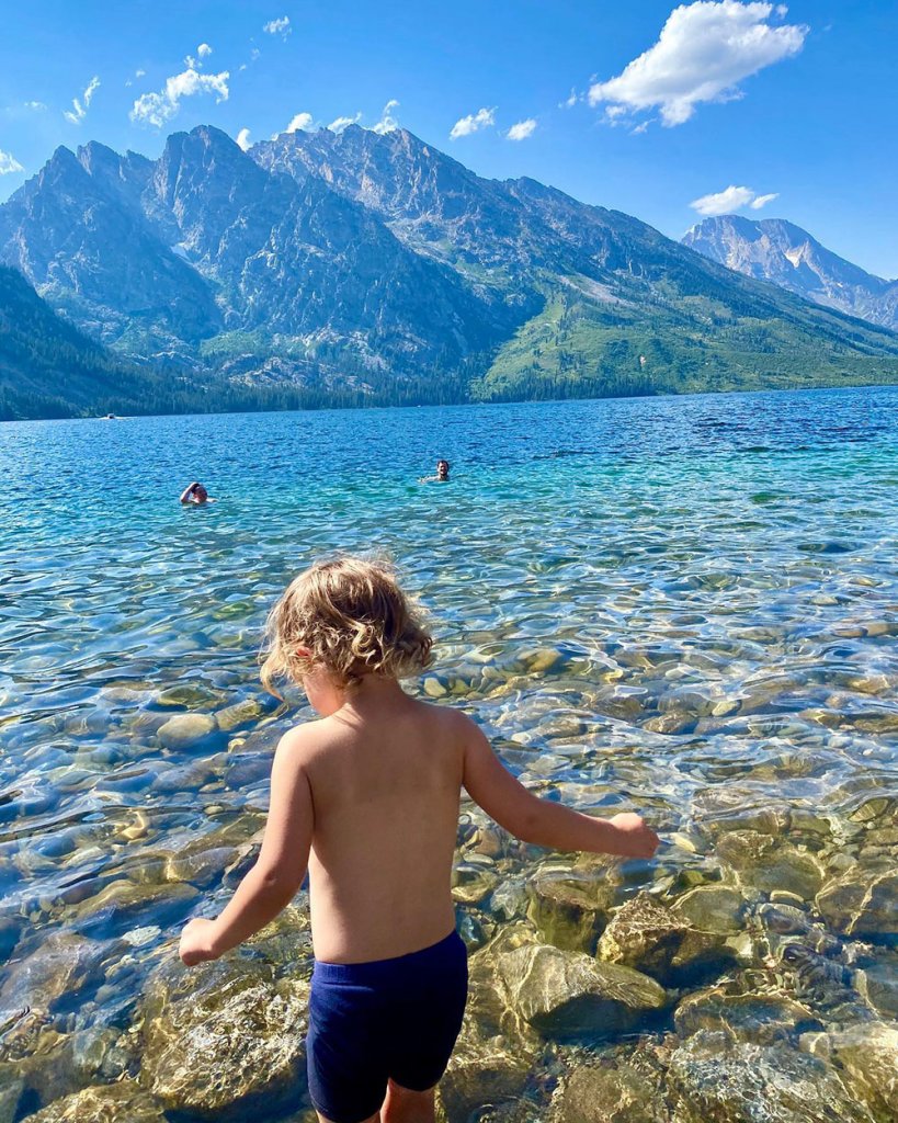 A child walks into the sparkling blue waters of Jenny Lake to go swimming in Grand Teton National Park.