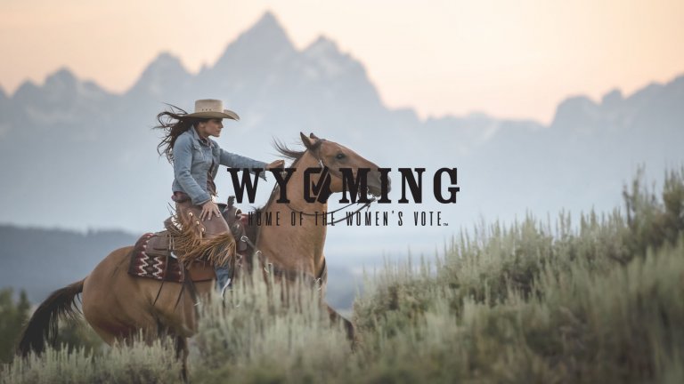 Woman riding horse in Grand Teton National Park with Women's Suffrage logo in black
