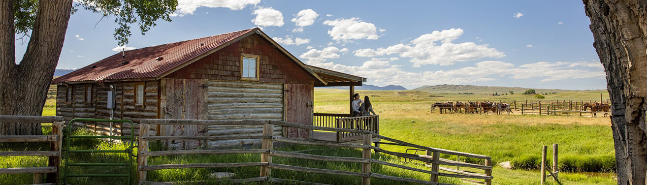 couple sitting on the corner of a porch looking out at the pasture of horses.