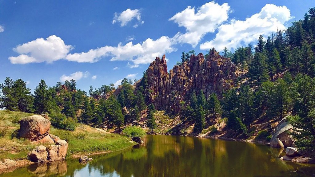 The river shines beneath the rocky terrain that's covered in green pine trees on a bright day at Curt Gowdy State Park. 