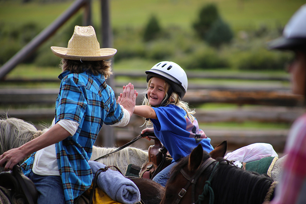 Man and little girl on horseback high fiving on a dude ranch in Wyoming 