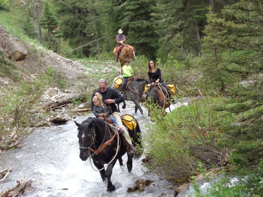 A family riding horses through a creek.