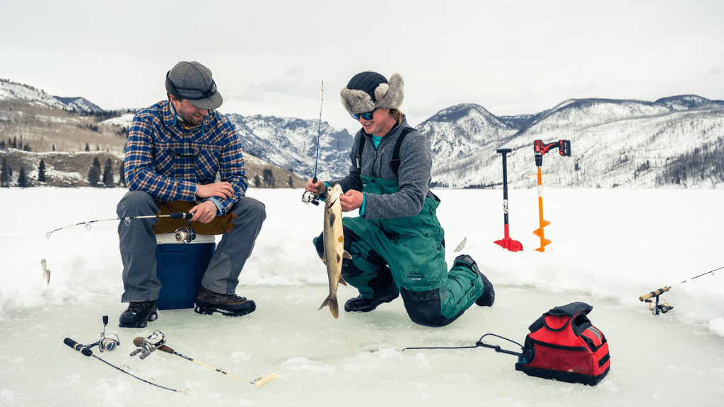 A couple guys ice fishing on a lake in the mountains.