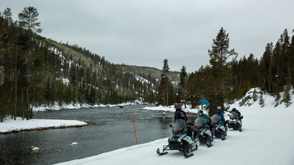A group of snowmobilers along a lake in Yellowstone National Park during the winter season. 