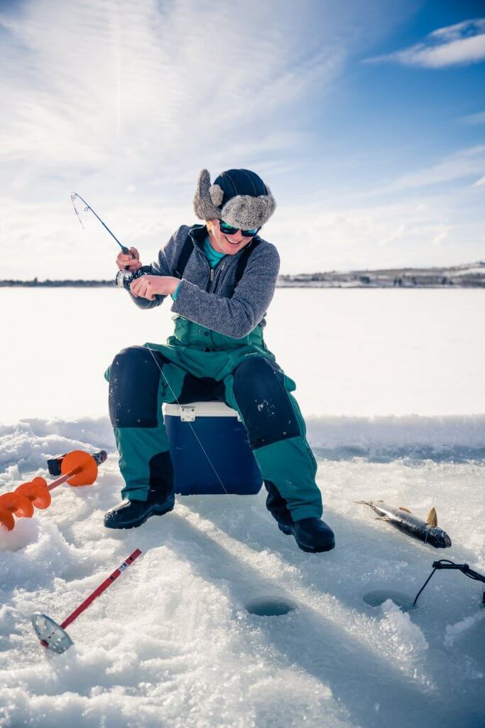 A man ice fishing at a lake in Grand Teton National Park during the winter 