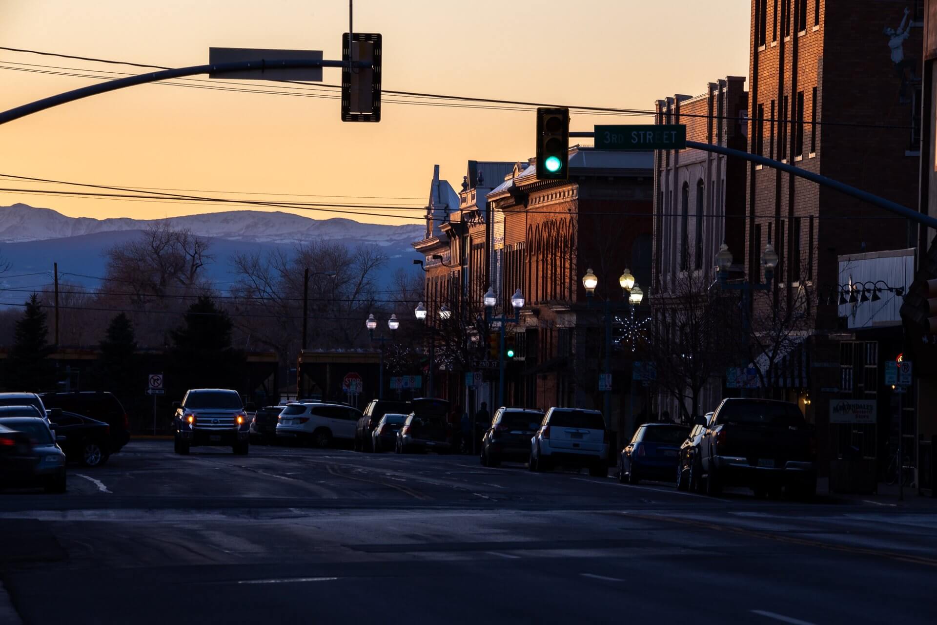 A golden sunset washes over the mountains in the city of Laramie as the traffic light glows green on the main street, where a car's lights blink in the distance. 