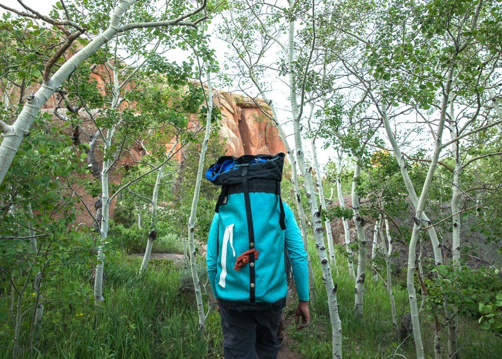 hiker with large backpack filled with climbing gear hikes through aspen trees at Vedauwoo