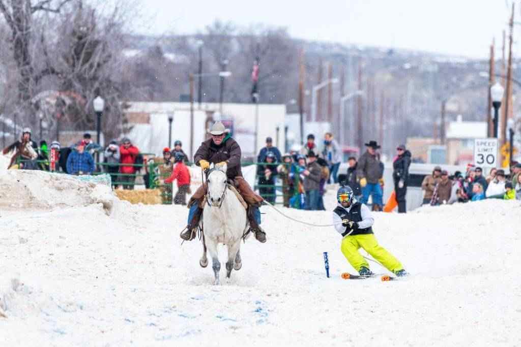 Man on skis being pulled by a horse and cowboy