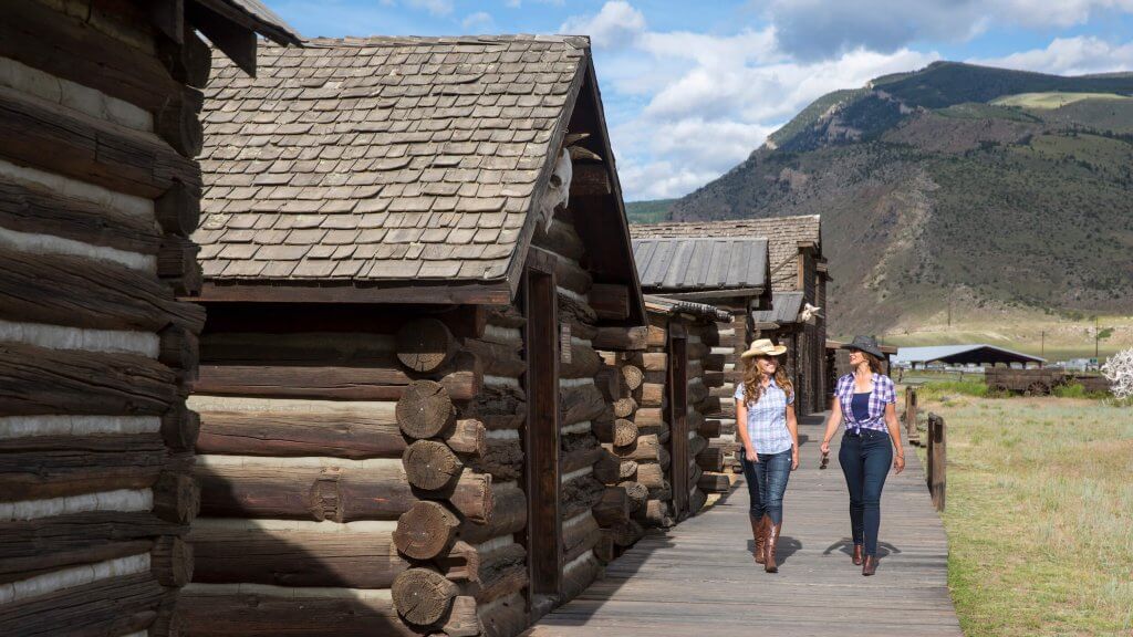 Two women walk alongside Old Trail Town, one of the top things to do in Cody WY, wearing cowboy hats and boots.