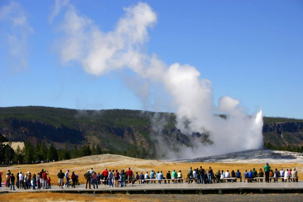 Hundreds of visitors gather around Old Faithful as its geyser erupts, one of the best things to do in Yellowstone and a must-see.