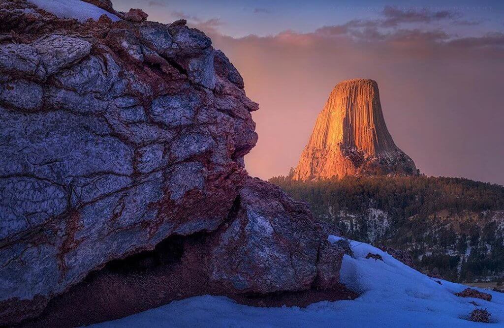 Devils tower bathed in pink shades of sunset contrasts against cool snow.