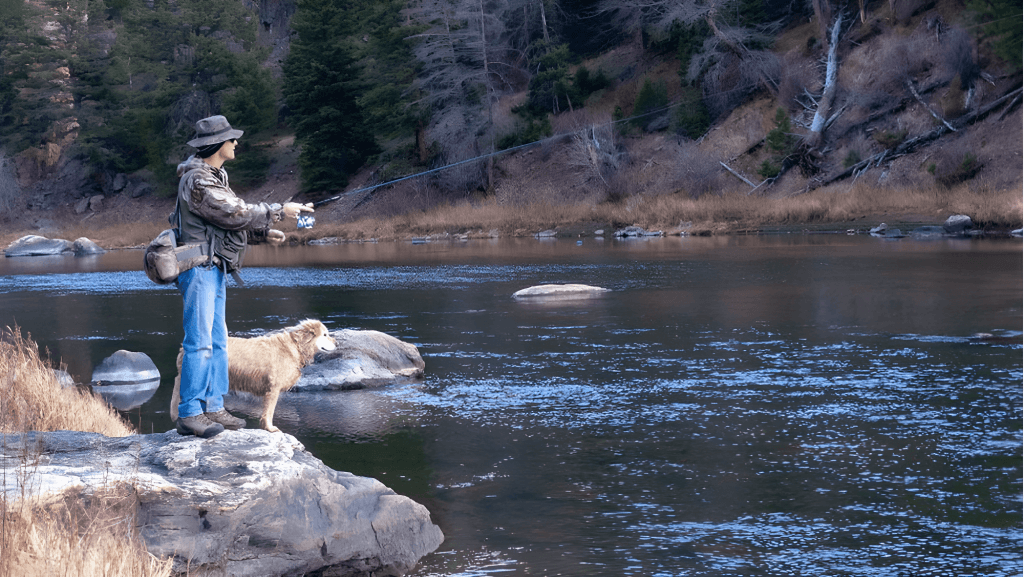 A person enjoying fly fishing in Saratoga, Wyoming with their loyal dog by their side, one of the many exciting things to do in the area.