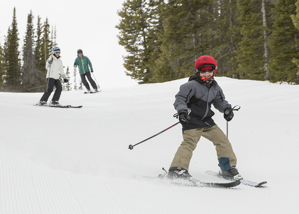 Family skiing downhill with smiles on their faces, a popular activity during winter vacations in Wyoming.