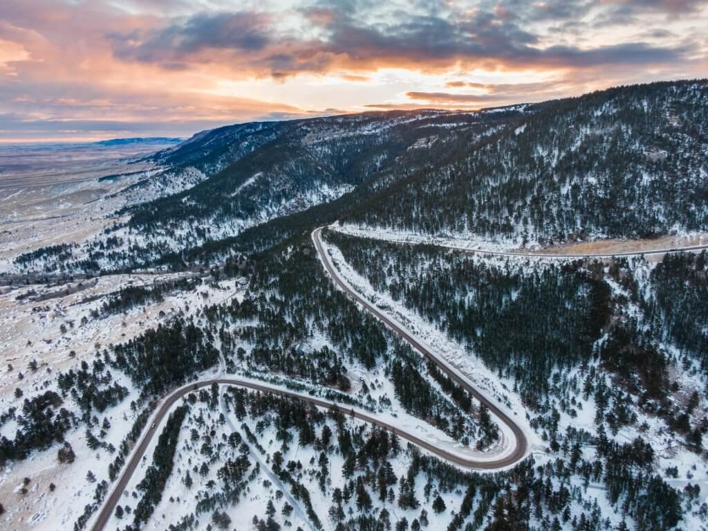 A winding road snakes through a snow-covered Casper Mountain during twilight, with warm hues in the sky above the chilly landscape.