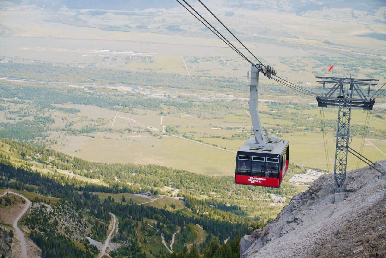 The Jackson Hole Aerial Tram making its way up Rendezvous Mountain and a sweeping landscape of forests and open plains below.