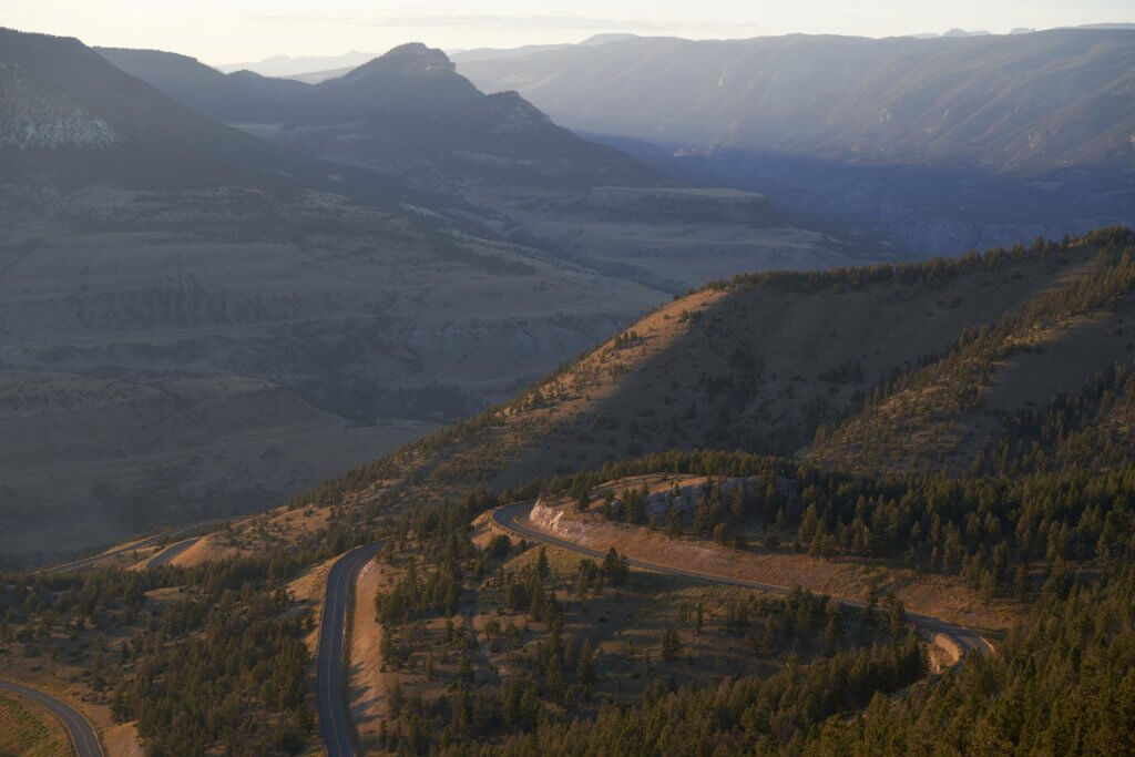 An overhead view of a scenic byway winding through a a hilly landscape covered with trees.