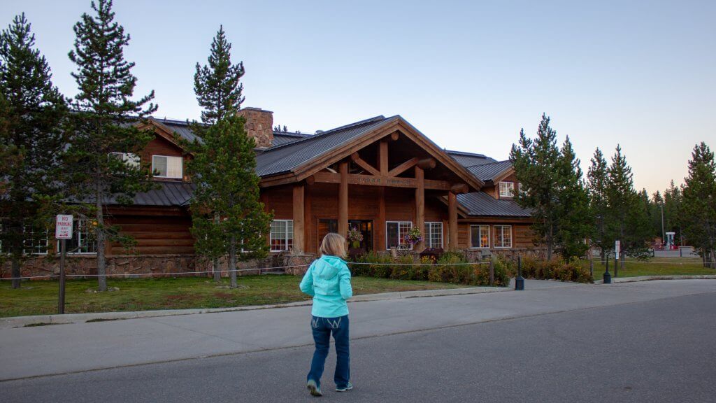 A child walking in front of wooden building surrounded by trees at Grand Teton National Park.