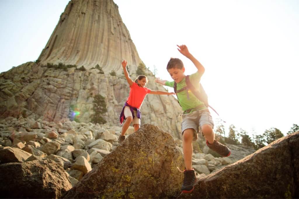 Two kids leap in the air, joyfully jumping on an adventure at Devils Tower National Monument in Wyoming.