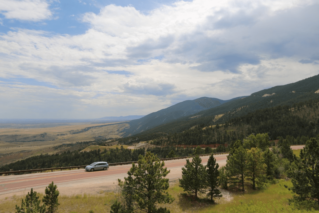 A car moves across the scenic street into Bighorn National Recreation Area as beautiful landscapes surround both sides with rolling hills, green trees and mountain views. 