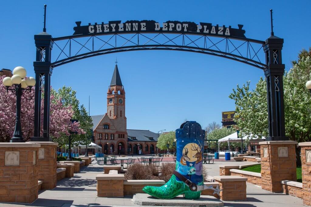 A colorful scene at Cheyenne Depot Plaza, where a painted cowboy boot stands in the middle of the courtyard as vibrant trees bloom in the background before big clock tower. 