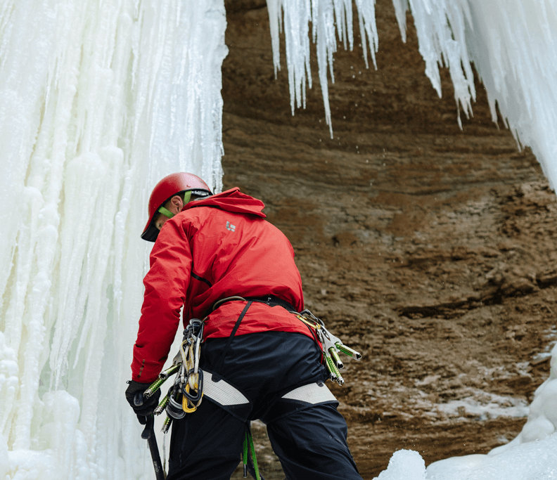 Aaron Mulkey in a red jacket and helmet standing next to a large icicles