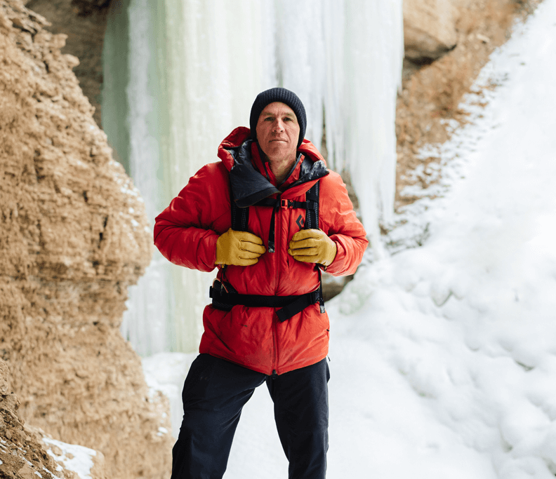 Aaron Mulkey in a red jacket and black hat standing in front of a frozen waterfall